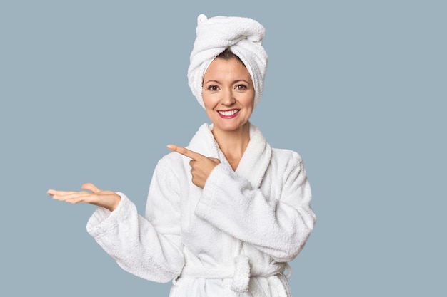 Caucasian woman in bathrobe and towel excited holding a copy space on palm