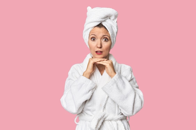 Caucasian woman in bathrobe and towel praying for luck amazed and opening mouth looking to front