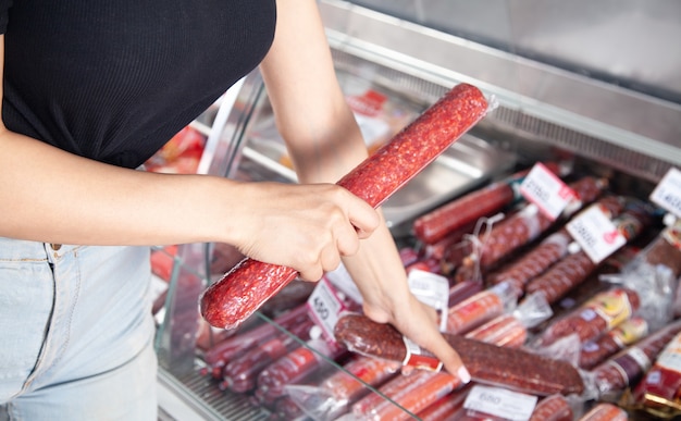 Caucasian woman buying sausage in supermarket.