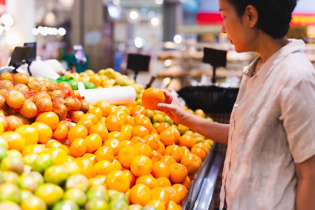 Кавказская женщина-потребительница в продуктовом магазине выбирает сочные апельсиновые цитрусовые