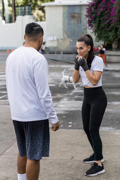 Caucasian woman in defense position in front of boxing trainer. Couple in a park exercising.