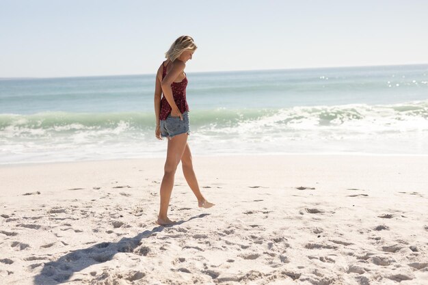 Caucasian woman enjoying her time at the beach with her friends on a sunny day, walking barefoot with hands in pocket