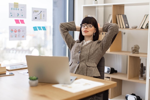 Caucasian woman in formal wear relaxing in office chair with arms behind head