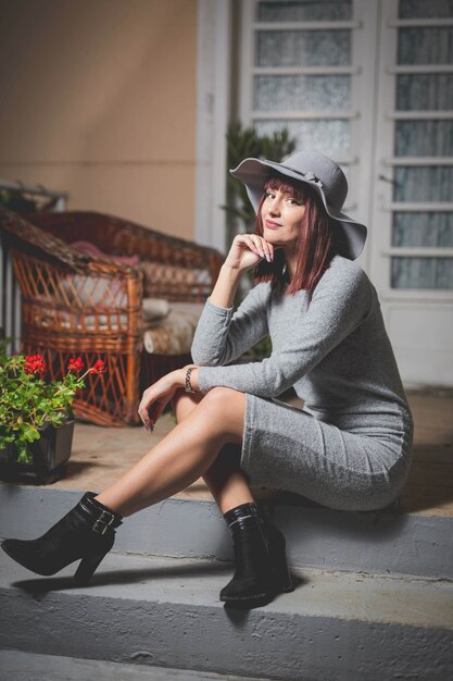 Caucasian woman in a gray hat and black tall boots posing on stairs leading to front door of house