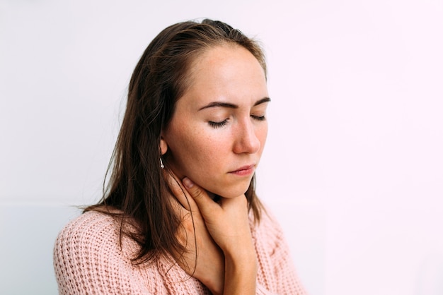 Caucasian woman has a cold and holds on to sore throat and neck.