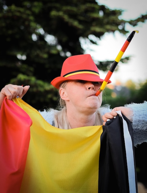 Caucasian woman holding a Belgian flag and blowing a whistle celebrating independence day