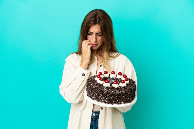 Donna caucasica che tiene la torta di compleanno isolata su fondo blu che ha dubbi