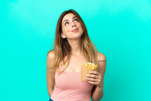 Caucasian woman holding fried chips isolated on blue background and looking up
