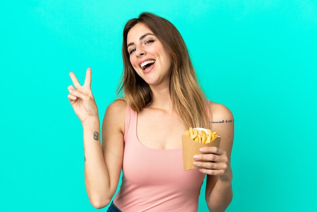 Caucasian woman holding fried chips isolated on blue background smiling and showing victory sign