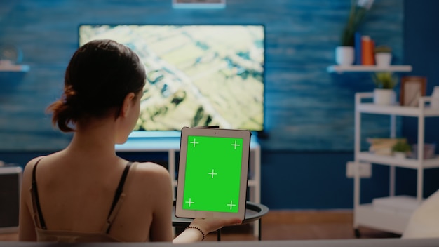 Caucasian woman holding green screen vertically on digital tablet