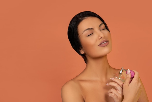 Caucasian woman holding perfume bottle on peach color background studio shot