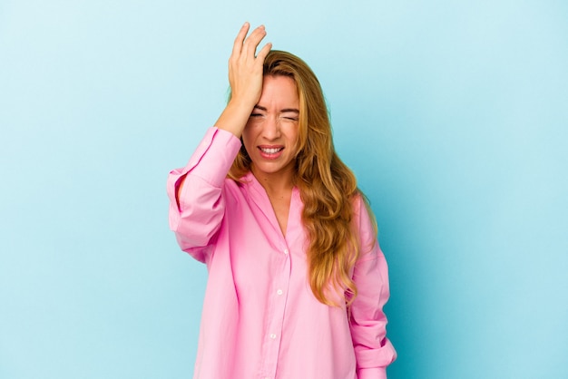 Caucasian woman isolated on blue background forgetting something, slapping forehead with palm and closing eyes.