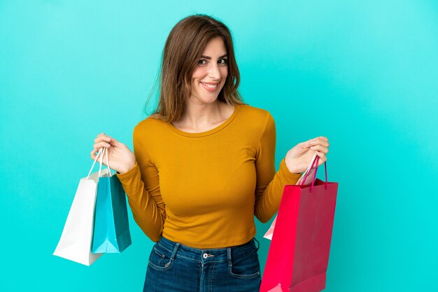 Caucasian woman isolated on blue background holding shopping bags and smiling