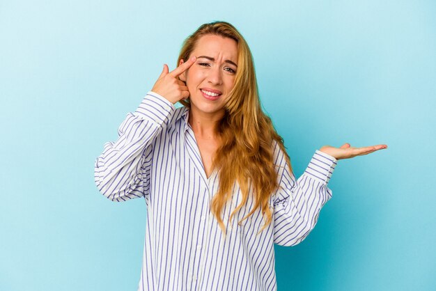 Caucasian woman isolated on blue background holding and showing a product on hand.