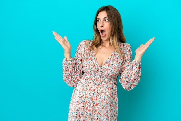 Caucasian woman isolated on blue background pregnant and doing surprise gesture