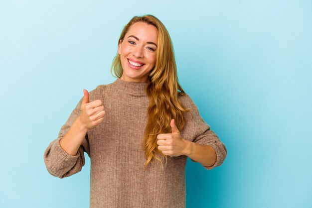 Caucasian woman isolated on blue background raising both thumbs up, smiling and confident.