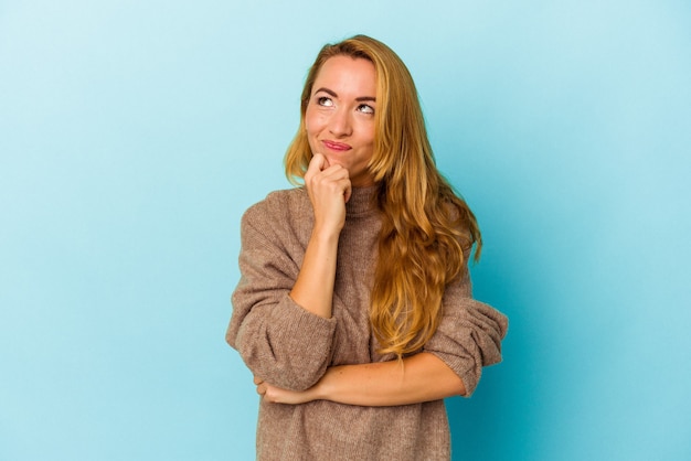 Caucasian woman isolated on blue background relaxed thinking about something looking at a copy space.