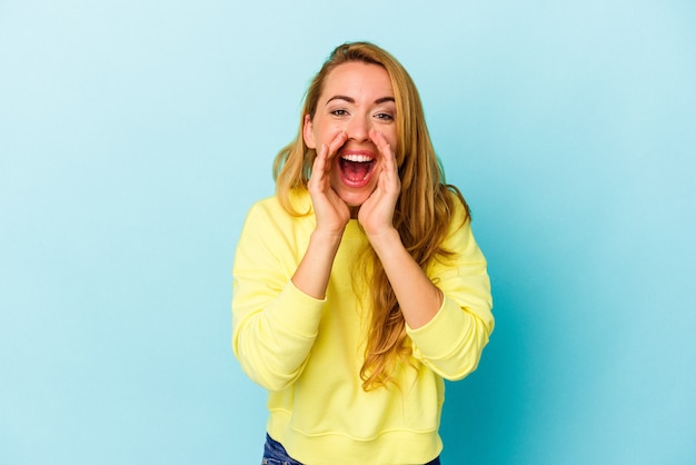 Caucasian woman isolated on blue background saying a gossip, pointing to side reporting something.