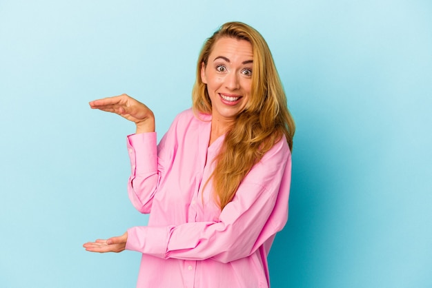 Caucasian woman isolated on blue background shocked and amazed holding a copy space between hands.