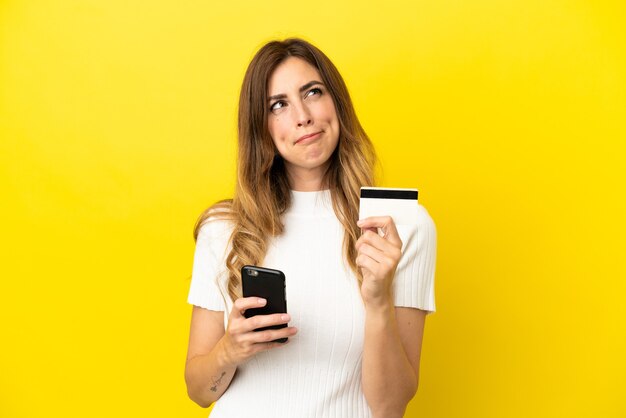 Caucasian woman isolated on yellow background buying with the mobile