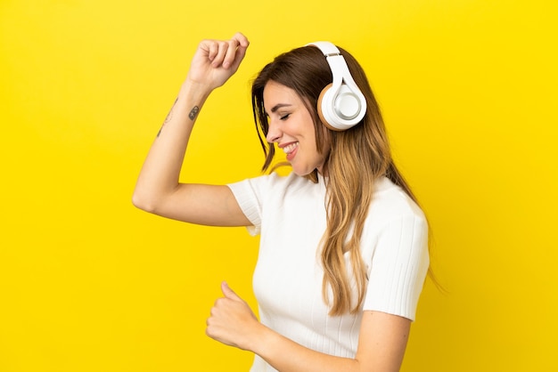 Caucasian woman isolated on yellow background listening music and dancing