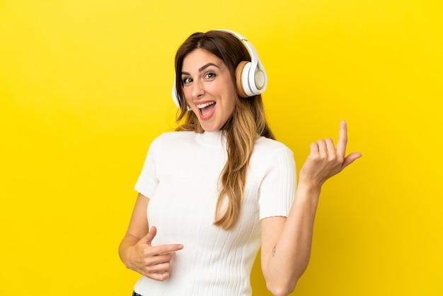 Caucasian woman isolated on yellow background listening music and doing guitar gesture