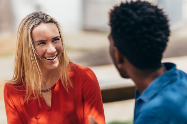 Caucasian woman laughs while talking to her boyfriend of African origin sitting on a bench