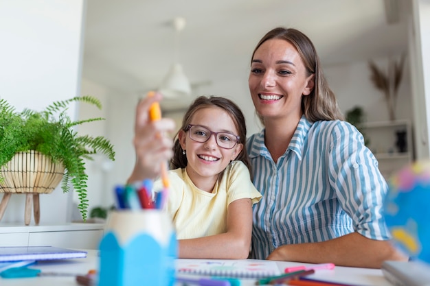 Photo caucasian woman looking proud at her daughter during homeschooling and doing some painting.