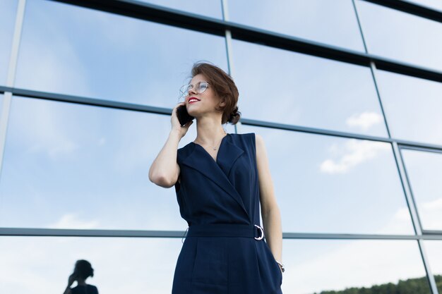 Caucasian woman in office clothes talking by telephone near the office building