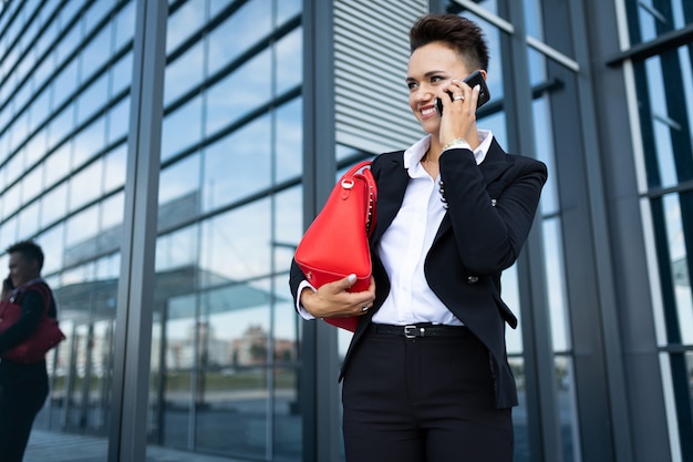 Caucasian woman in office clothes and with red bag waits colleague near office building