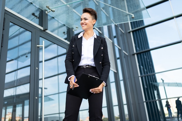 Caucasian woman in office clothes with tablet waits colleague near the office building