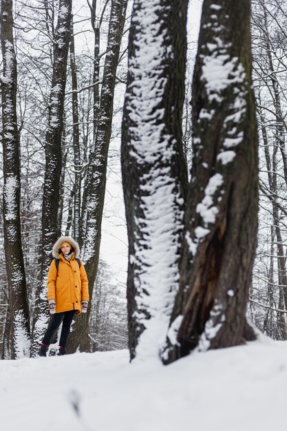 Caucasian woman in orange jacket walking in a winter park in the middle of the trees in nature, enjoying the walk and the winter scenery and silence