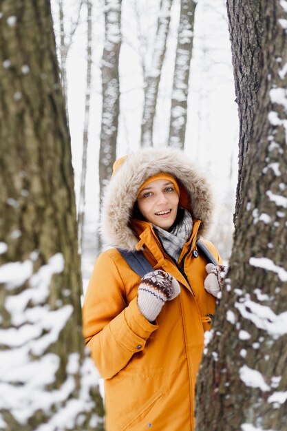 Caucasian woman in orange jacket walking in a winter park in the middle of the trees, portrait of a woman in nature, who enjoys a walk and the winter landscape