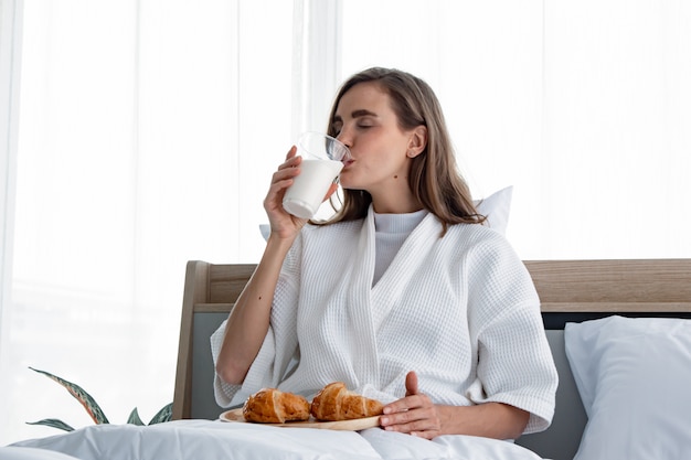 Caucasian woman in pijama ready to eat breakfast is milk and croissants in the morning