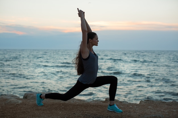 Yoga di pratica della donna caucasica alla spiaggia dell'oceano