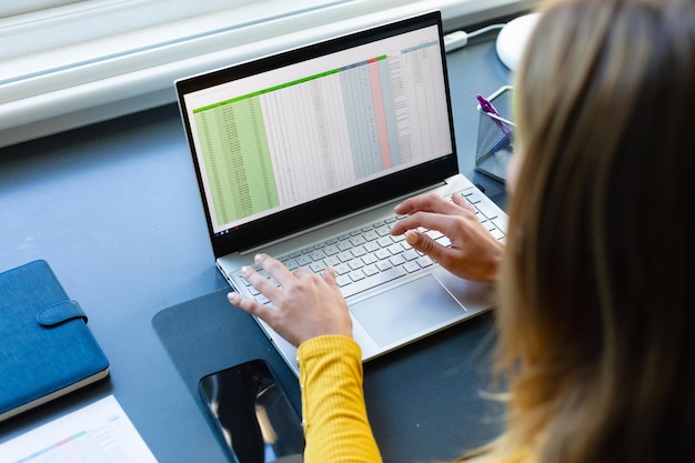 caucasian woman sitting at desk working from home and using laptop in sunny room