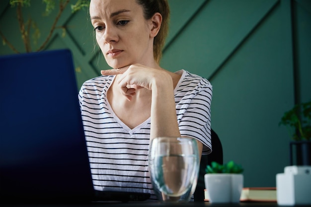 Photo caucasian woman sitting at table at home office and works with laptop freelancer remotely working