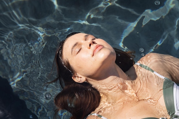 Кавказская женщина проводит время у бассейна, самоизолируясь, расслабляясь в воде в бассейне. Социальное дистанцирование в условиях карантина во время эпидемии коронавируса ковид 19.