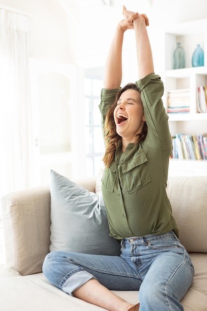 Caucasian woman spending time at home, sitting on sofa, stretching her arms. lifestyle at home isolating, social distancing in quarantine lockdown during coronavirus covid 19 pandemic