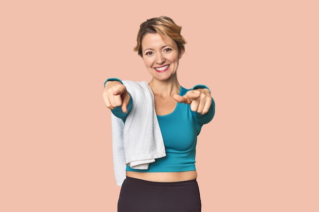 Caucasian woman in sportswear with towel cheerful smiles pointing to front