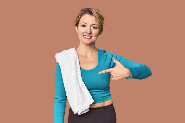 Caucasian woman in sportswear with towel person pointing by hand to a shirt copy space proud