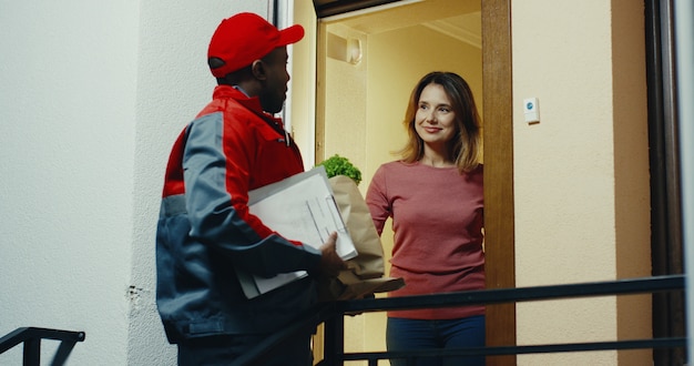 Caucasian woman taking her delivery of the fresh vegetables from the supermarket from the courier and signing for that. Inside.