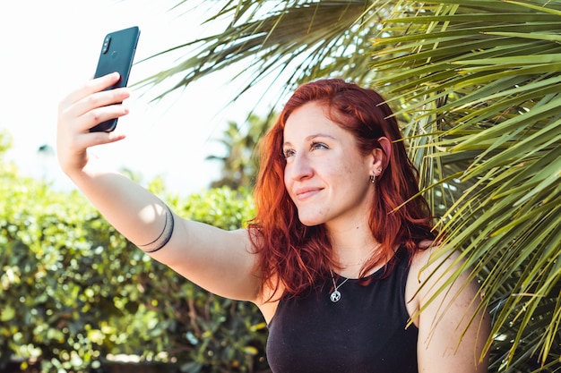 백인 여자 야외 공원에서 스마트 폰으로 selfie를 복용