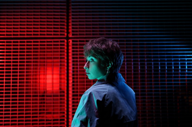 Caucasian woman turning head to side stands with back to camera\
next to wall with red blue neon glow