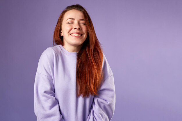 Caucasian woman in violet sweatshirt Natural look Smiling long red hair Violet background