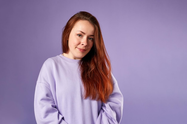 Caucasian woman in violet sweatshirt Natural look Smiling long red hair Violet background