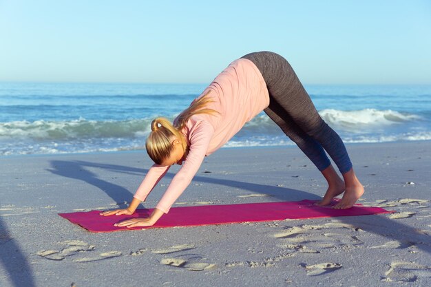 A Caucasian woman wearing sports clothes, enjoying time at the beach on a sunny day, practicing yoga, stretching in yoga position