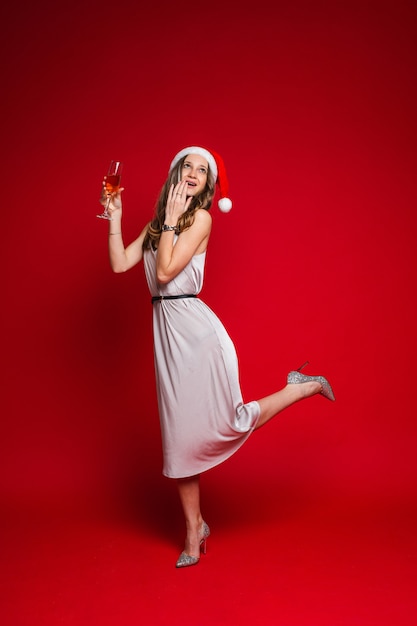 Caucasian woman with attractive appearance holds a glass of white wine, picture isolated on red wall