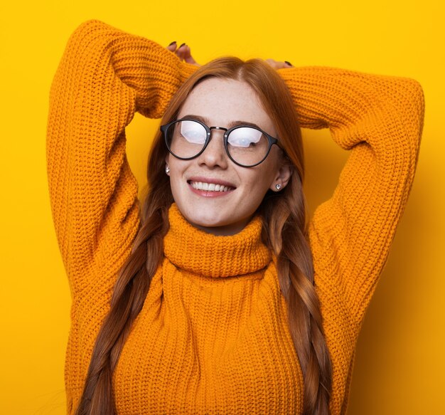 Caucasian woman with eyeglasses and freckles smiling at camera in a knitted yellow sweater