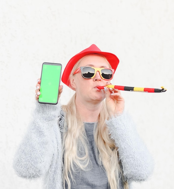 Foto donna caucasica con un cappello che soffia la bandiera belga tende la mano tenendo un telefono cellulare